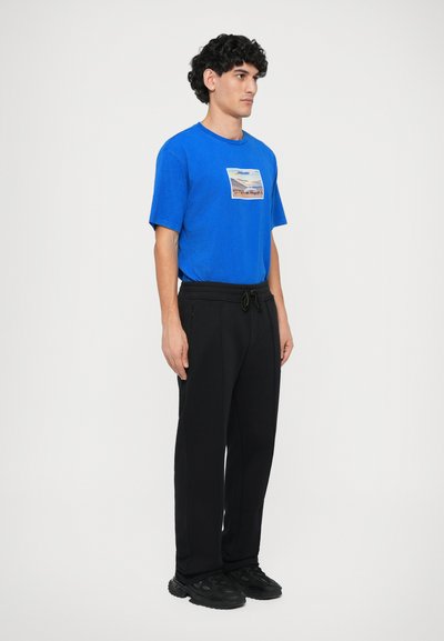 Blue T-shirt with a graphic print, paired with black jogger pants featuring a drawstring waist, and black shoes with textured accents.