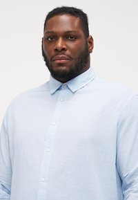 Chemise boutonnée à manches longues bleu clair en coton, dotée d'un col classique et de petits boutons blancs le long de l'avant.