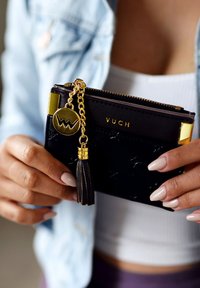 Černá syntetická peněženka se zlatými detaily, vybavená zipem, řetízkovým třásněním a logem. Hladký povrch, kompaktní design pro snadné používání.