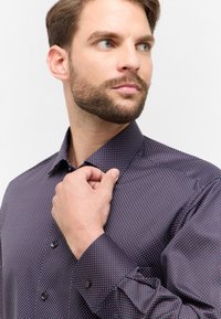 Donkerpaars overhemd met een klein blauw en rood stippenmotief. Voorzien van een klassieke kraag en knopenmanchetten, gladde textuur.