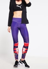 Fioletowe legginsy sportowe z kolorowym, abstrakcyjnym wzorem z czerwonymi i niebieskimi detalami, wykonane z elastycznego materiału, w połączeniu z czarnym topem i kurtką.
