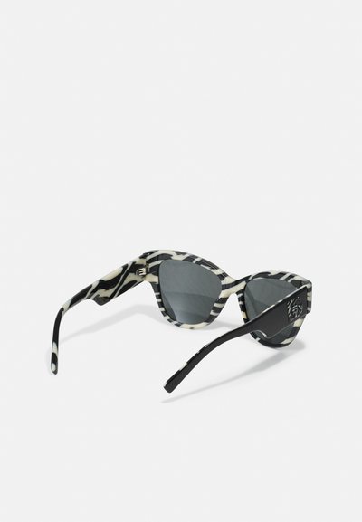 Ochelari de soare tip cat-eye cu un model zebra alb-negru, lentile gri și brațe negre solide cu detalii ale logo-ului pe tampla.
