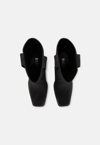 Bottines noires avec un bout carré, texture lisse et un détail de sangle arrière. L'intérieur présente la marque "RAID" en argent.