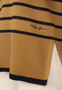 Pull en tricot couleur moutarde avec des rayures horizontales bleu marine. Présente un ourlet à côtes et des fentes sur les côtés. Logo de la marque brodé en bleu marine.