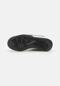 Green and white athletic shoe sole, featuring a textured black rubber bottom with a circular groove and brand logo in green.