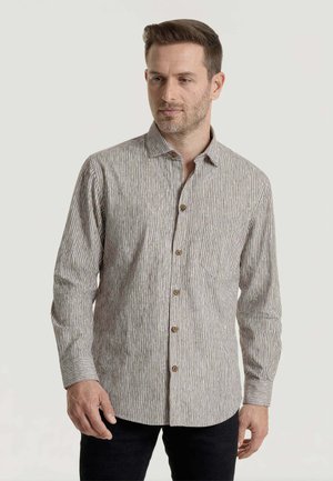 Uomo che indossa una camicia a maniche lunghe, a righe bianche e grigio chiaro con bottoni marroni, in piedi davanti a uno sfondo semplice.