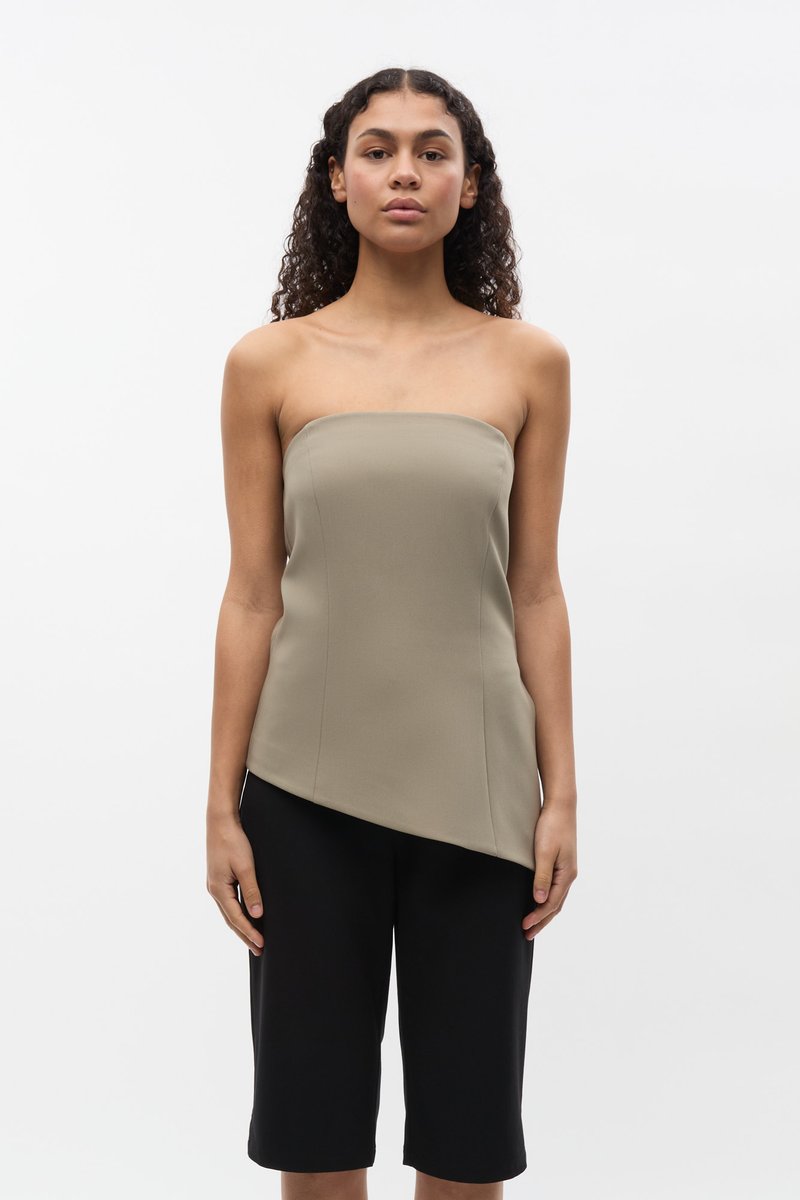 Top sin tirantes en color beige, confeccionado con una tela suave y con un dobladillo asimétrico. Combinado con pantalones cortos negros de altura hasta la rodilla.