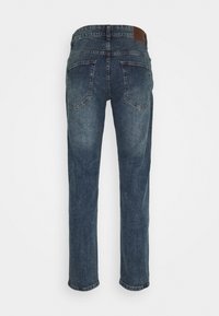 Jeans de denim azul oscuro con dos bolsillos traseros y una etiqueta de marca de cuero marrón en la cintura, mostrados desde la parte trasera.
