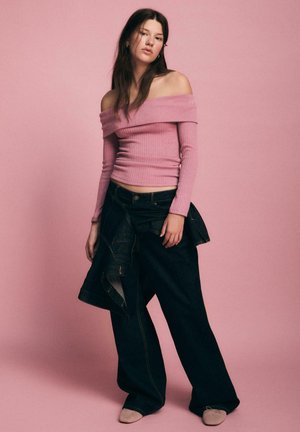 Tætsiddende, off-shoulder, ribbet pink top parret med løse, mørke denim bukser med et lagdelt design. Bløde beige fodtøj fuldender looket.
