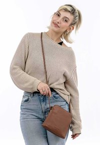 Pull en maille beige avec texture côtelée, associé à un jean bleu clair. Un petit sac en cuir marron à bandoulière avec fermeture éclair est accroché à une sangle.