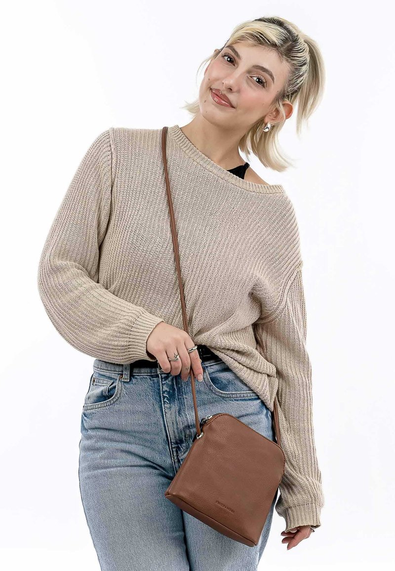 Pull en maille beige avec texture côtelée, associé à un jean bleu clair. Un petit sac en cuir marron à bandoulière avec fermeture éclair est accroché à une sangle.