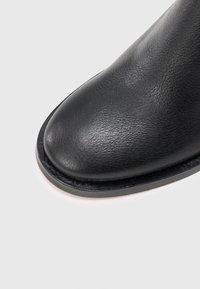 Juodas odinis botas su apvaliu pirštu ir tekstūruota paviršiumi, pasižymintis elegantišku, lygiais dizainu ir subtilia briauna prie pado.