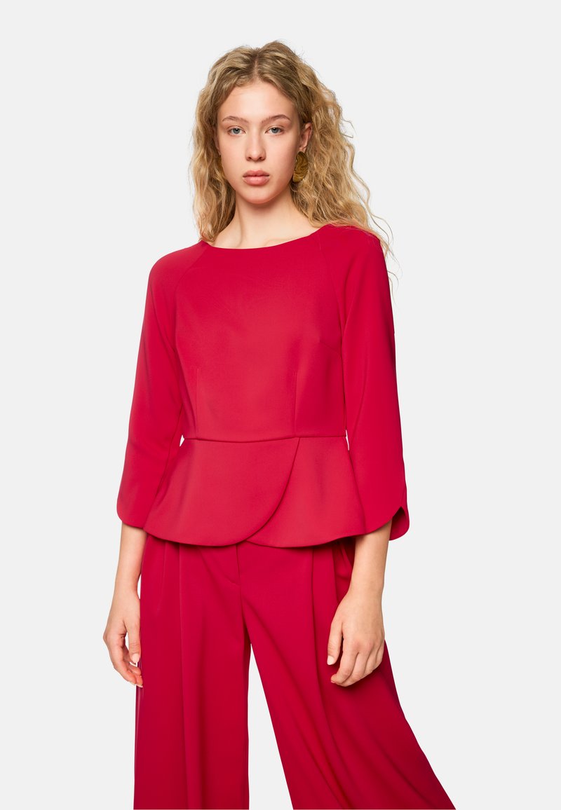 Rotes Peplum-Top aus leichtem Stoff mit langen Ärmeln und rundem Halsausschnitt, das eine glatte Textur und einen ausgestellten Saum hat.