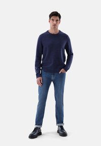 Maglione di lana blu navy con scollo a girocollo, abbinato a jeans azzurri chiari. Il modello indossa stivali neri con lacci e suola spessa.