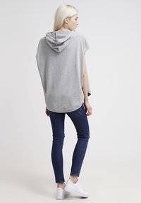 Felpa leggera grigia con maniche corte, orlo curvo e cappuccio. Abbinata a jeans skinny blu scuro e sneakers bianche.