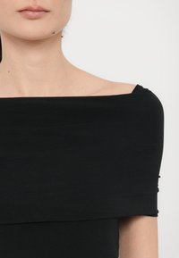 Zwarte off-the-shoulder top met een zachte stof en minimalistisch design, met accent op een getailleerde silhouet en strakke lijnen.