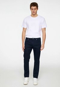 Temno modre ozke kavbojke z sprednjimi žepi in zapiranjem na gumb. Kombinirane z belo bombažno majico in belimi supergami.