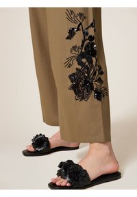 Zwarte sliders met een gestructureerde bloemdecoratie, gecombineerd met losse khaki broek met zwarte bloem broderie en pailletten.