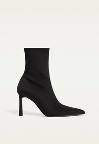 Bottine noire en tissu lisse avec un bout pointu et un talon aiguille haut. Présente un design sans couture et une couture texturée.