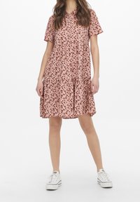 Rosa blommig klänning med korta ärmar, skiktad kjol, knäppning framtill och små bruna blommönster. Kombinerad med vita sneakers.