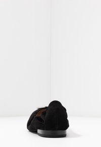 Sorte ruskind flade sko med rund tå, lav sort hæl og dekorativt sølvhardware på overdelen. Glat overflade.