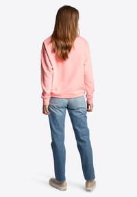 Sudadera rosa de mangas largas, corte relajado y puños acanalados, combinada con jeans de color azul claro y zapatos beiges. Modelo mostrado de espaldas.