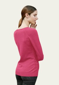 Pull ajusté rose en tissu doux, avec des manches longues et un col rond, doté d'un ourlet côtelé et de détails en tricot à cables sur les côtés.