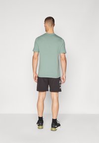 T-shirt vert menthe à manches courtes avec un col rond, associé à un short noir portant un texte blanc et des baskets noires avec des accents verts.
