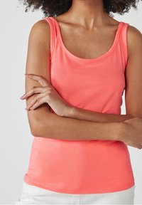 Débardeur corail sans manches fabriqué en tissu doux, présentant un col arrondi et une coupe ajustée. Texture lisse sans motifs ni accents.