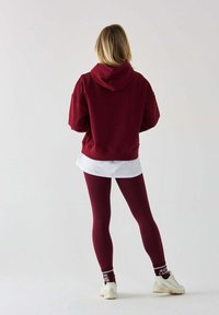 Bordowa bluza z kapturem, zestawiona z bordowymi leggingsami o fakturze. Pod spodem biała warstwowa koszula. Stylizowana z białymi trampkami i wzorzystymi skarpetkami.