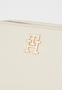 Cremefarbene, strukturierte Lederbörse mit einer goldfarbenen Logo-Plakette, die die ineinander verschlungenen Buchstaben zeigt. Mit Reißverschluss an der Oberseite.