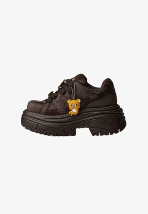 Fetter dunkelbrauner Sneaker mit dicker Sohle, strukturiertem Obermaterial und einem kleinen gelben Bären-Schlüsselanhänger, der an den Schnürsenkeln befestigt ist.
