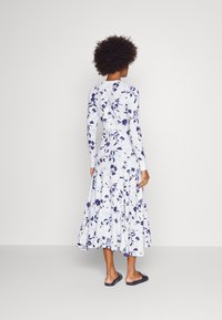 Robe à manches longues à fleurs blanches avec des fleurs bleu marine. Jupe évasée et tissu doux. Portée avec des sandales noires à enfiler.