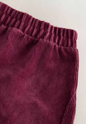 Burgundské kordové joggingové kalhoty s vroubkovaným elastickým pasem a texturovanou tkaninou, která má vertikální žebrování a jemné povrchové detaily.