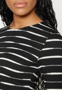 Randig stickad topp i svart och vitt med rund halsringning och texturerad tyg, med ojämna horisontella ränder och ribbat avslut.