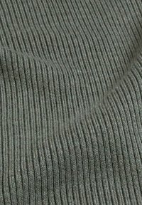 Geribbelde stof in gedempte groentinten, met fijne verticale strepen. Gelaagd oppervlak met zachte, licht harige vezels.