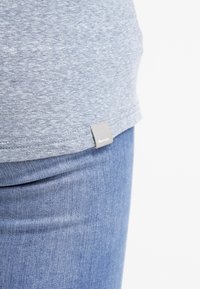 T-shirt grigio melange con etichetta cucita all'orlo. Abbinato a jeans in denim azzurro chiaro con una trama liscia.