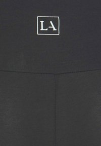 Black activewear leggings with ribbed texture, featuring a white square logo "LA" on the waistband. Minimalist design, form-fitting style.