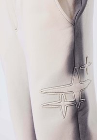 Primo piano di pantaloni chiari con design a stelle ricamate e sfumature degradè lungo la cucitura laterale.