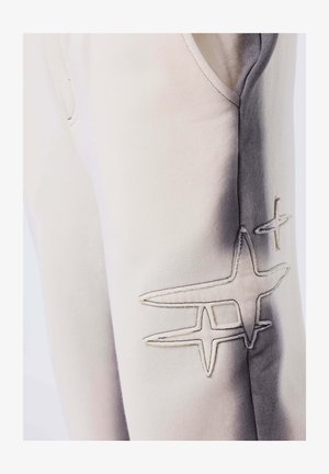 Close-up of light-colored pants with stitched star designs and gradient shading along the side seam.