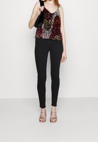 Top in paillettes con motivi multicolore, pantaloni skinny neri e tacchi rosa con cinturini. L'accessorio è una piccola borsa nera in pelliccia sintetica.