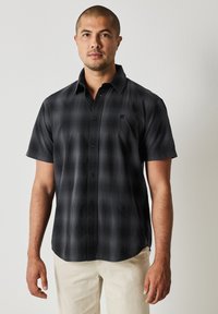 Kortärmad skjorta i svart och grå rutigt mönster, tillverkad av ett mjukt tyg, med en knapp-ner krage och en liten logodetalj på bröstet.