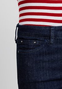 Midjeområdet av mörkblå denimjeans som bärs med en röd och vit horisontellt randig skjorta.