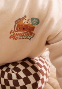 Beige sweatshirt with a cute pumpkin pie graphic and the text "Pumpkin Pie Bake Sale" above brown and beige checkered pants.