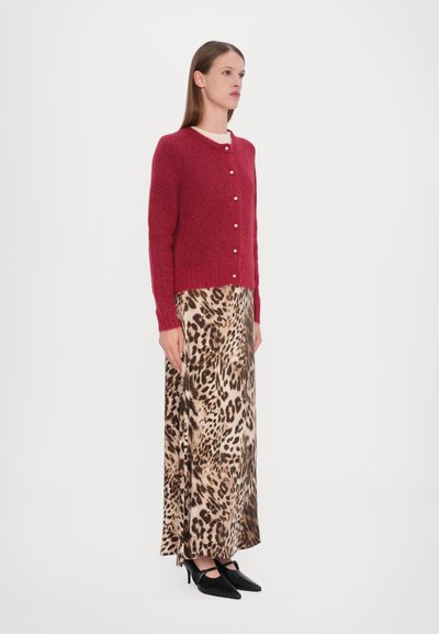 Cardigan rosso in pelliccia sintetica con scollo rotondo e chiusura a bottoni, abbinato a una gonna lunga con stampa leopardata e tacchi a punta neri.