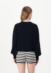 Marineblå cropped sweatshirt med lange ærmer, parret med højtaljede sort-hvide stribede ribbede shorts. Simpelt design, uden udsmykninger.