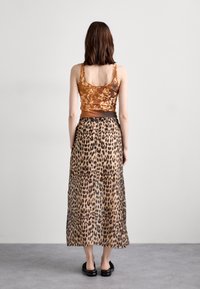 Brun mönstrad tanktop som matchas med en lång leopardmönstrad kjol. Kjolen har en följsam textur och en bred midjeband. Svarta platta skor.