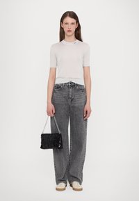 Top corto a maniche corte grigio chiaro a coste con scollatura rotonda e sottile accentatura del logo. Abbinato a jeans grigi a vita alta e vestibilità morbida e a una borsa nera con paillettes.