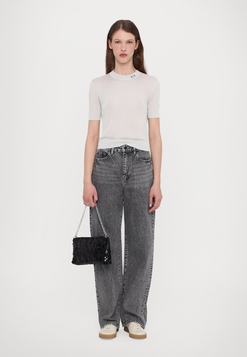 Top corto a maniche corte grigio chiaro a coste con scollatura rotonda e sottile accentatura del logo. Abbinato a jeans grigi a vita alta e vestibilità morbida e a una borsa nera con paillettes.