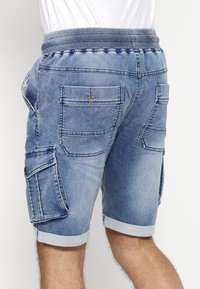 Blå denim shorts med elastisk talje, flere lommer og opbrettede kanter. Stoffet har en faibet vask med syninger som detaljer.